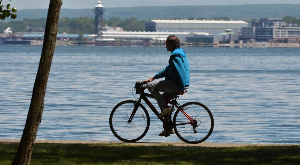 A cyclist rides along the multipurpose trail at Presque Isle State Park near Erie, background, on May 11. Presque Isle Bay sits between the popular park and Erie.