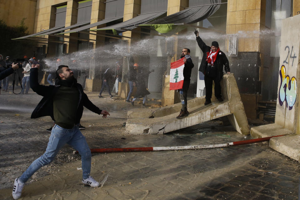 Anti-government demonstrators throw stones toward riot police during a protest against a parliament session for a vote of confidence for the new government in downtown Beirut, Lebanon, Tuesday, Feb. 11, 2020. (AP Photo/Bilal Hussein)