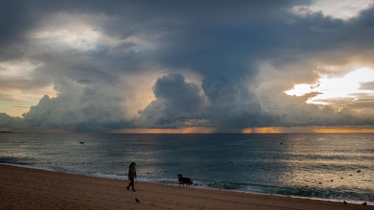 A woman walking a dog on a beach at sunset