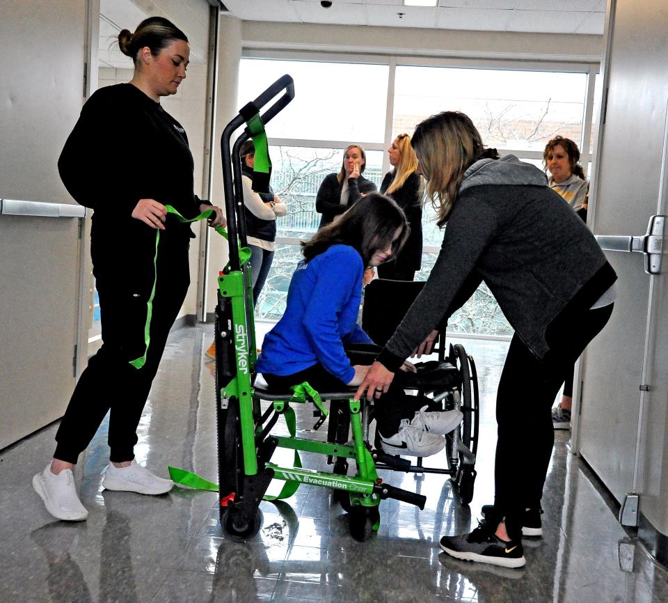 Makayla Maxwell, an eighth grade Wooster student, is transferred from her wheelchair to the evacuation chair by Julia Jurgenson and Michelle Stitt to demonstrate how the chair can be used to move people up and down stairs in an emergency.