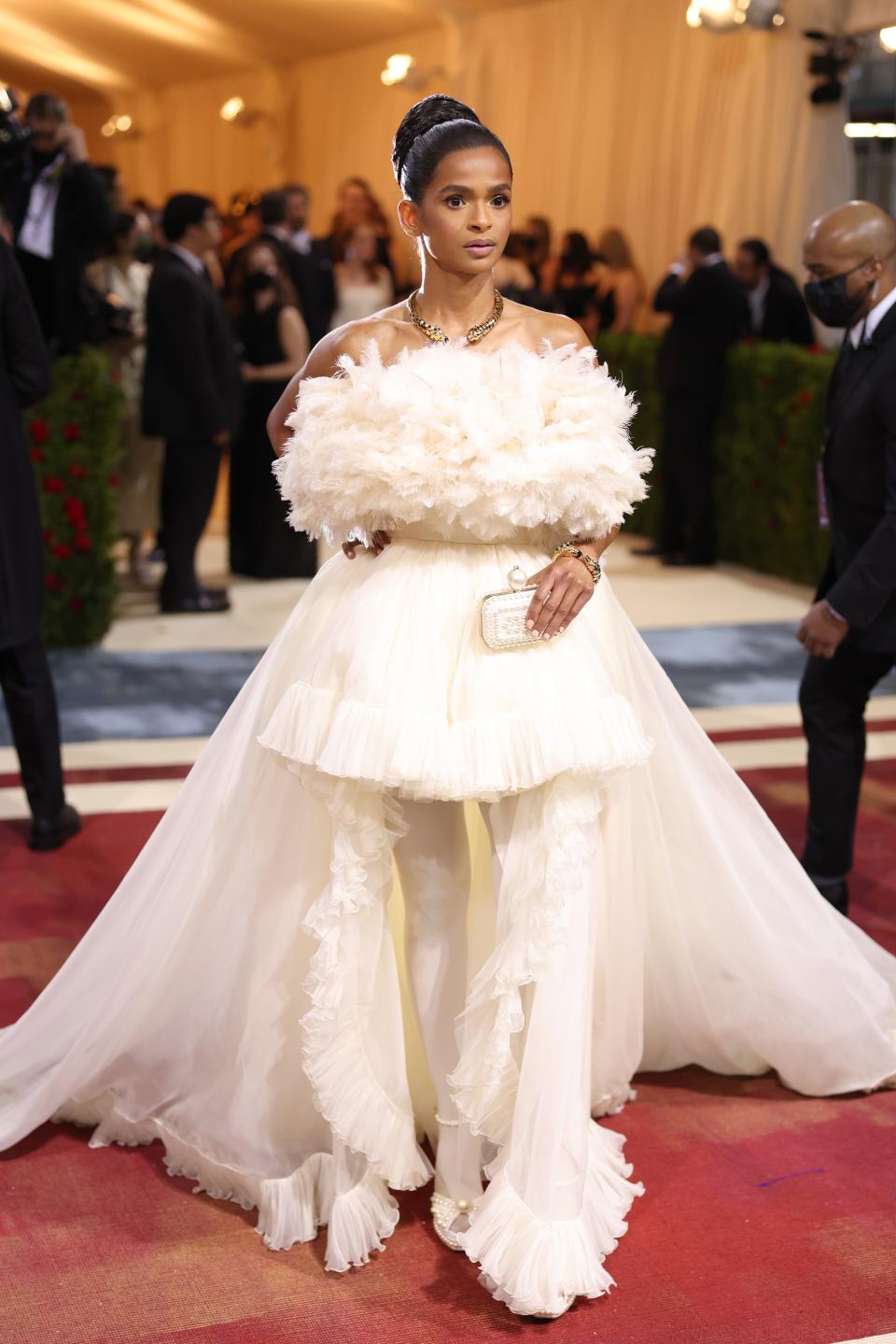 Ramla in an ivory white gown with a voluminous off-the-shoulder feather bodice, tulle miniskirt with more tull fabric flowing to the floor and into a large train.