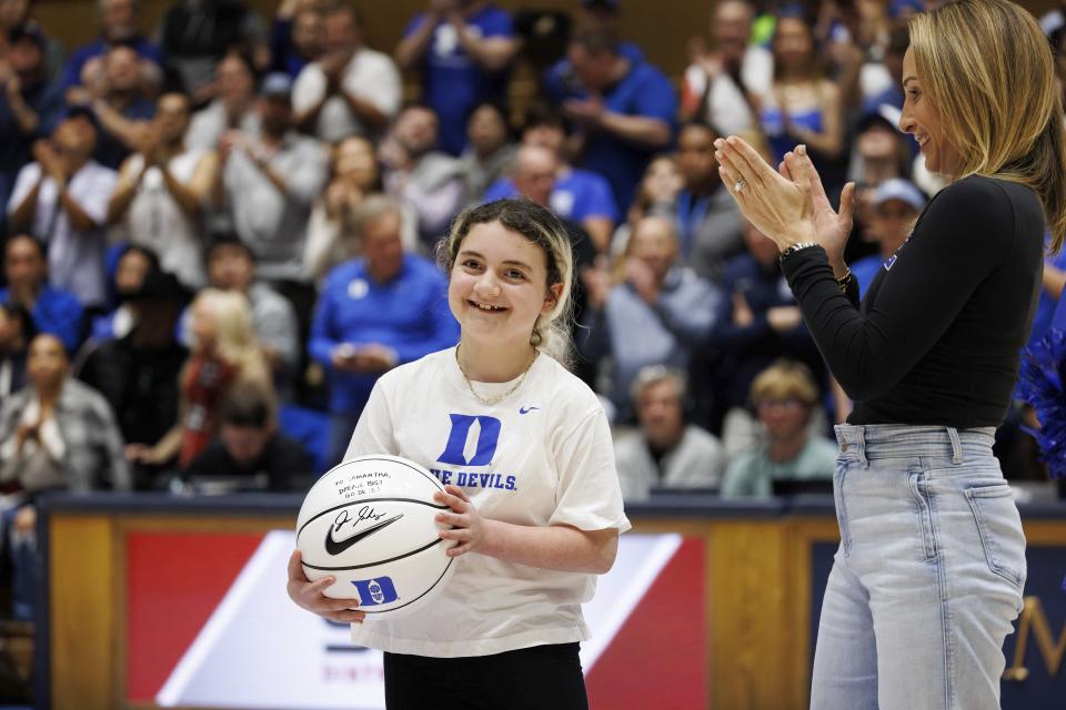 Marcelle Scheyer, right, wife of Duke coach Jon Scheyer, applauds after presenting a basketball signed by coach Scheyer to Samantha DiMartino as an honoree of the Scheyer Family Kid Captain Program, which recognizes patients and families of Duke Children's Hospital, during a timeout in an NCAA college basketball game between Duke and Louisville in Durham, N.C., Wednesday, Feb. 28, 2024. (AP Photo/Ben McKeown)