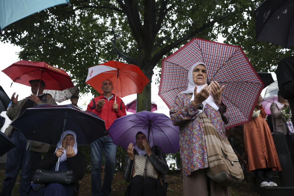 Men and women pray next to the truck carrying 50 coffins with remains of the victims of the 1995 Srebrenica genocide in Visoko, Bosnia, Friday, July 8, 2022. The remains of the 50 recently identified victims of Srebrenica Genocide will be transported to the Memorial centre in Potocari where they will be buried on July 11, the anniversary of the Genocide. (AP Photo/Armin Durgut)