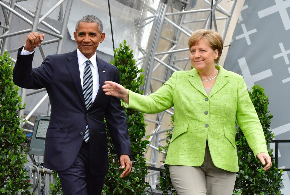 Barack Obama and Chancellor Angela Merkel wave as they arrive on stage during the Protestant Church Day event at the Brandenburg Gate in Berlin on May 25, 2017.