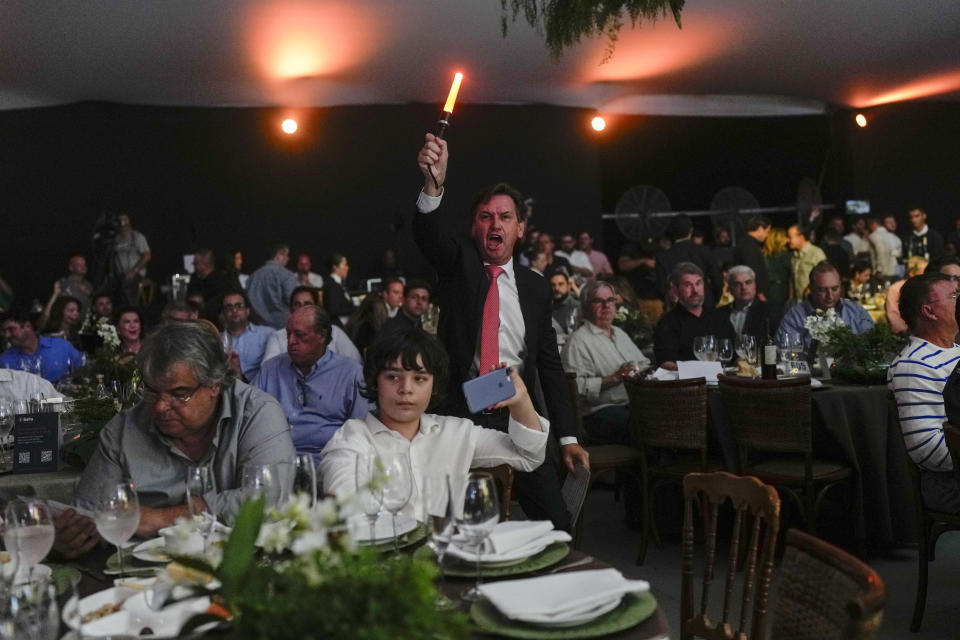 A spotter waves a light stick to signal receipt of a new bid at the Elo de Raça auction in Uberaba, Minas Gerais state, Brazil, Sunday, April 28, 2024. The Elo de Raça is the most prestigious auction taking place on the sidelines of the annual ExpoZebu, which bills itself as the world’s biggest Zebu fair. (AP Photo/Silvia Izquierdo)