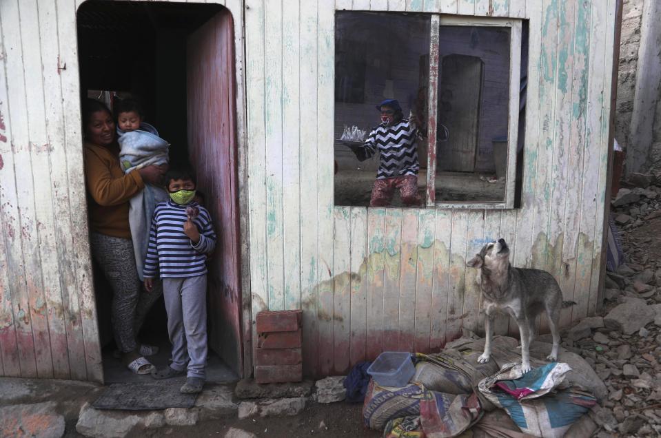 El payaso de circo Jhona Zapata, cuyo nombre artístico es "Jijolin", se refleja en la ventana de una casa mientras ofrece manzanas caramelizadas a la venta durante el cierre de los circospor la cuarentena para frenar la propagación de COVID-19 en un barrio pobre de las afueras de Lima, Perú, el miércoles 5 de agosto de 2020. (AP Foto/Martín Mejía)