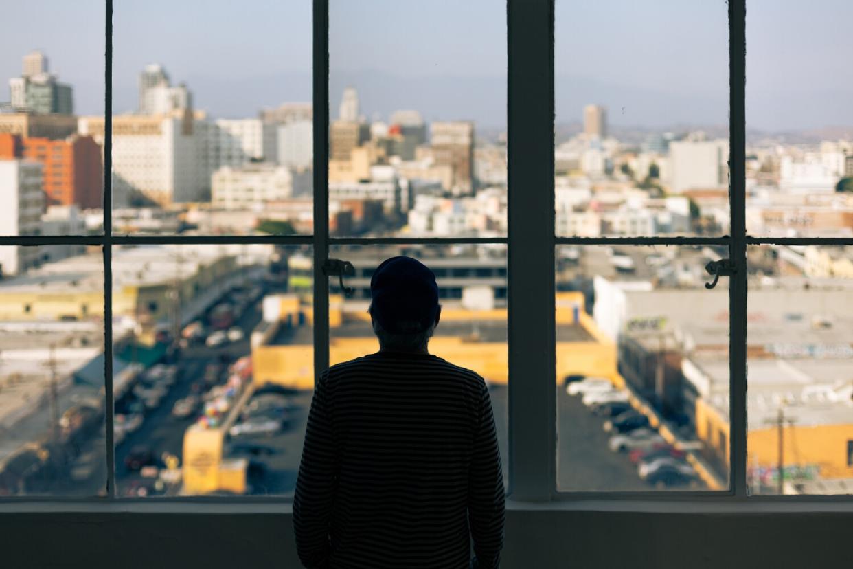 Robbie Conal, seen in silhouette, stands at a window overlooking downtown Los Angeles