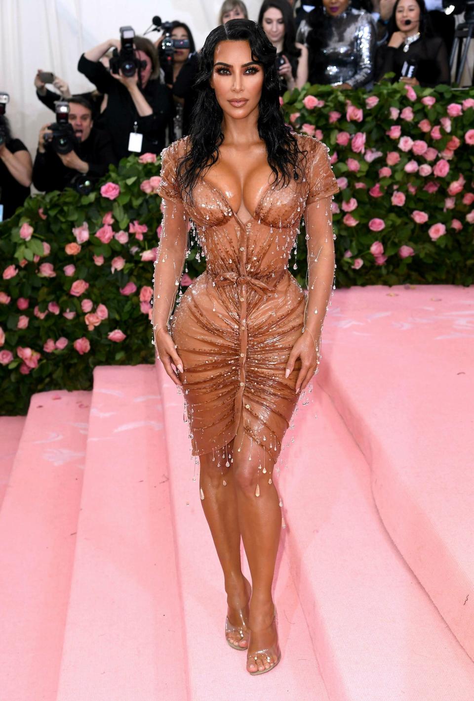 Kim Kardashian poses for photos on the 2019 Met Gala carpet wearing a formfitting nude gown with crystal raindrop embellishments.