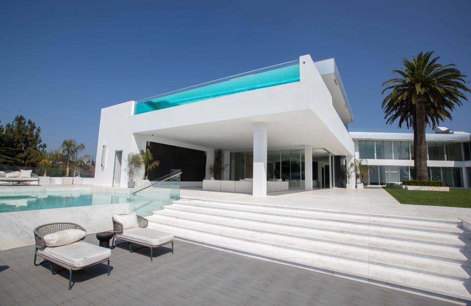 white chairs at the foot of stairs leading to a white building with a pool on the roof at mansion The One Bel Air