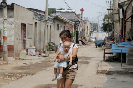 A woman carrying a boy walks along a street in Xiaozhangwan village of Tongzhou district, on the outskirts of Beijing, China June 28, 2017. Picture taken June 28, 2017. REUTERS/Jason Lee