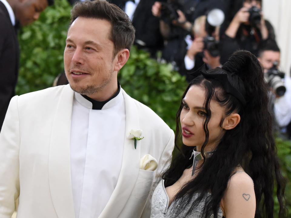 Elon Musk (left) and Grimes (right) standing next to each other and posing for photographers.