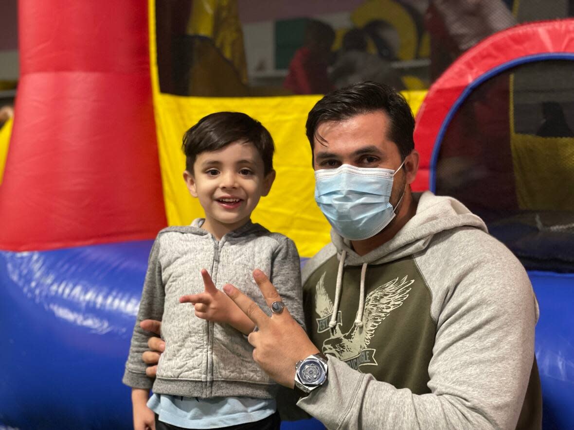 Out of breath from jumping on the bouncy castle, Sultan Tokhi's five-year-old son holds up the peace sign next to his father. (Meg Roberts/CBC - image credit)