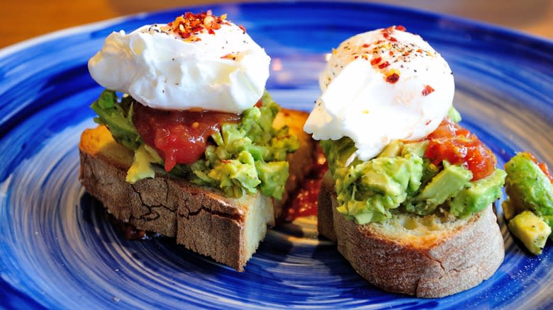 avocado toast with poached eggs and salsa roja on a blue plate