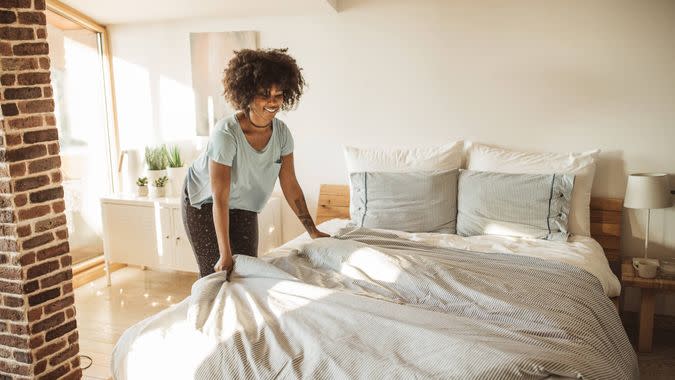 Young woman making bed at home.