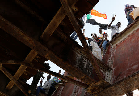 Sudanese protesters wave a national flag and make victory signs as they stand on a railroad bridge outside the defence ministry compound in Khartoum, Sudan, April 24, 2019. REUTERS/Umit Bektas