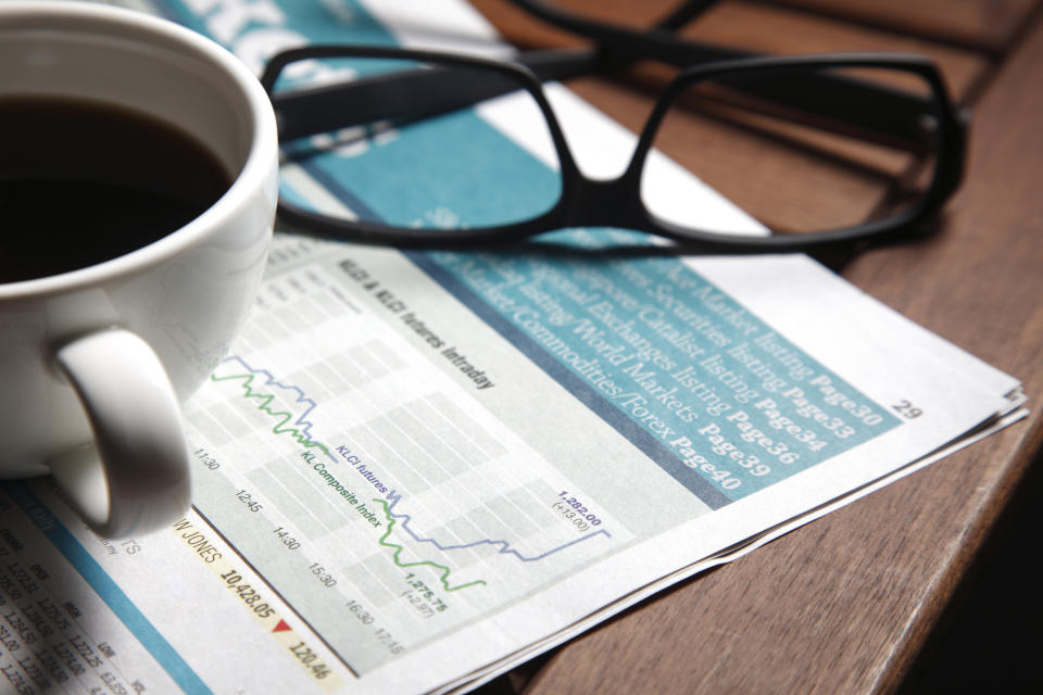 A coffee mug and glasses sit on top of a financial newspaper.