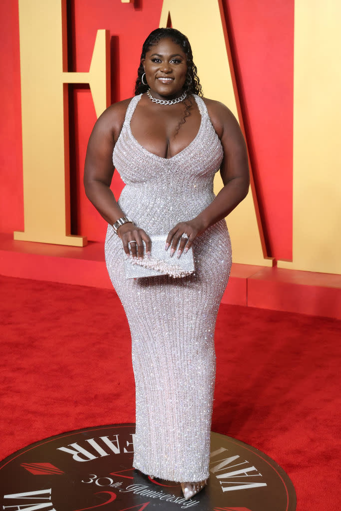 Person on red carpet in sparkling sleeveless dress with V-neckline and chain necklace