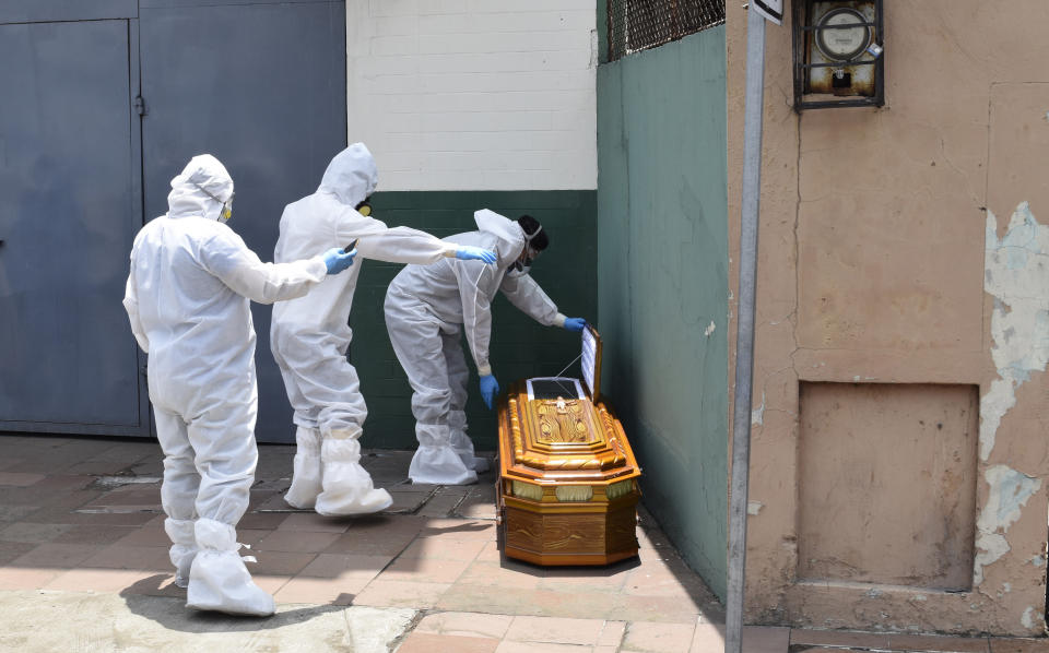 ARCHIVO – En esta fotografía de archivo del 6 de abril de 2020, trabajadores con equipo protector contra el coronavirus recogen un féretro que contiene los restos de un cuerpo al lado de una casa en Guayaquil, Ecuador. (AP Foto/Edison Choco, Archivo)