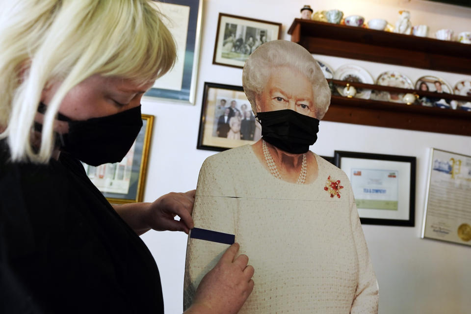 Molly Carew, manager of Tea & Sympathy, a British restaurant and shop, places a black arm band on a cardboard cutout of Queen Elizabeth II, to mourn the death of Britain's Prince Philip in New York, Friday, April 9, 2021. (AP Photo/Richard Drew)