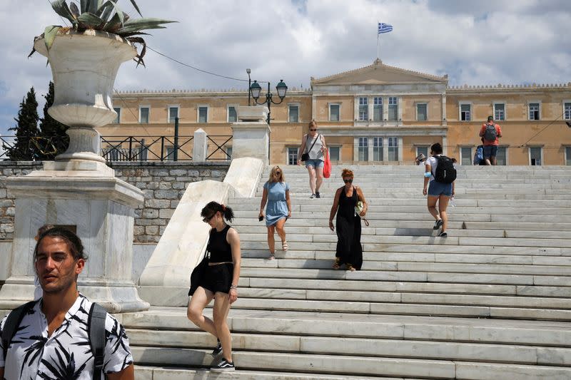 People make their way on Syntagma square, as the Greek parliament building is seen in the background in Athens