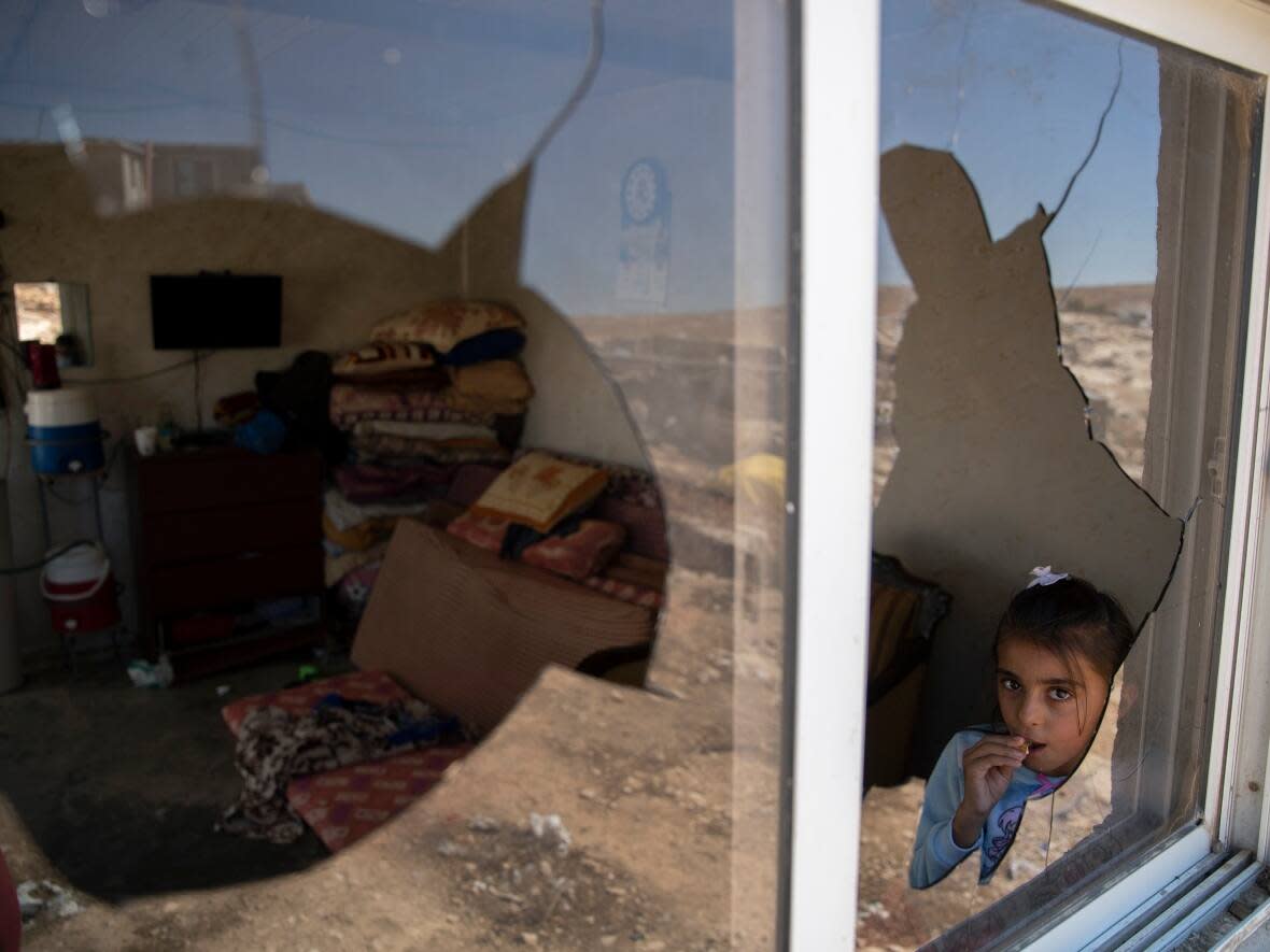 A Palestinian girl looks through her family home's shattered window after a settlers' attack in the West Bank village of al-Mufagara, near Hebron, on Thursday, Sept. 30, 2021. (Nasser Nasser/Associated Press - image credit)