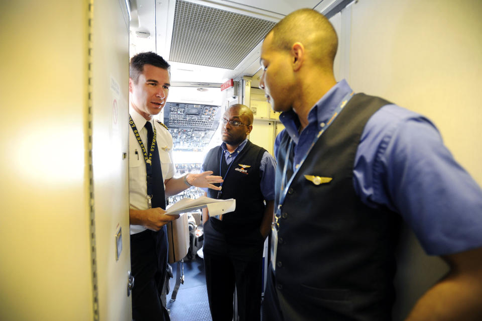 In this Thursday, May 9, 2013, photo, an Allegiant Air Capt. Bret Whalen, left, discusses the flight plan with flight attendants Antron Johnson, center, and John Taylor before their flight to Laredo, Tex, at McCarran International Airport in Las Vegas. While other U.S. airlines have struggled with the ups and downs of the economy and oil prices, tiny Allegiant Air has been profitable for 10 straight years. (AP Photo/David Becker)