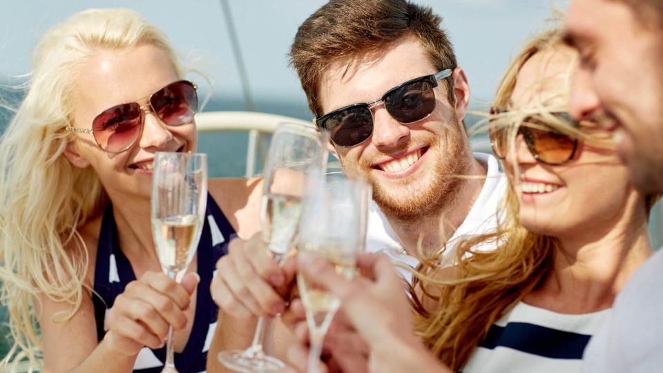 vacation, travel, sea, friendship and people concept - smiling friends with glasses of champagne on yacht.