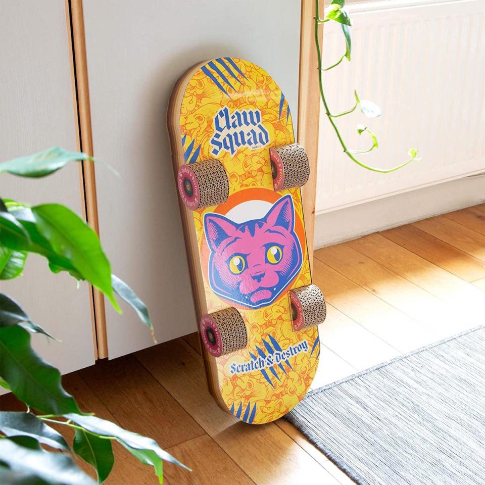 A yellow cat scratching post shaped liked a skateboard propped up against a wall near a glass door