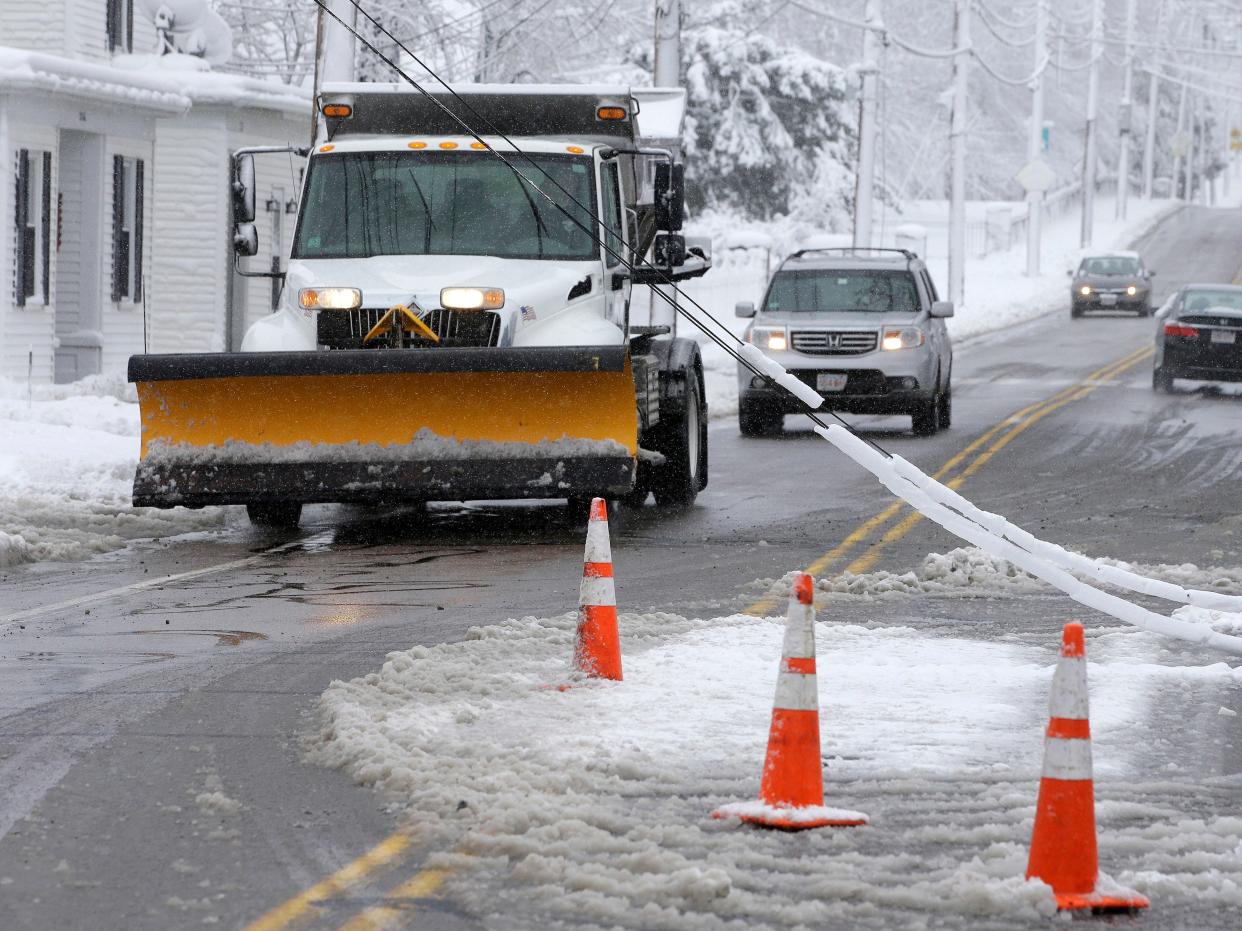 A snowplow drives past downed power lines, Thursday, March 8, 2018, in Walpole, Mass.