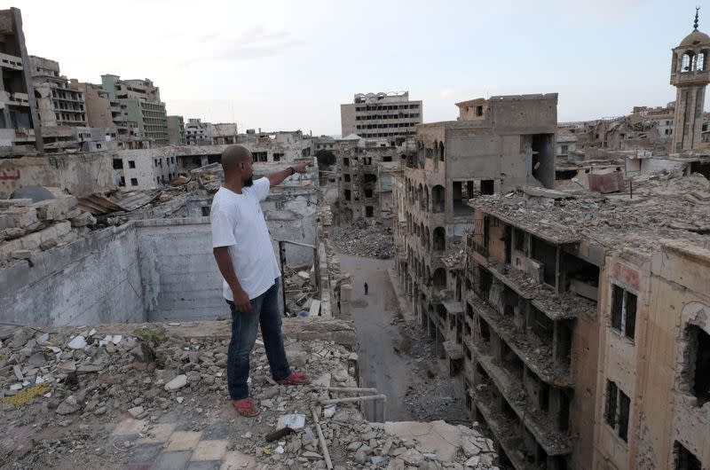 Malik Abdullah Ali reacts as he stands on the damaged roof of the building where he lives, in Benghazi