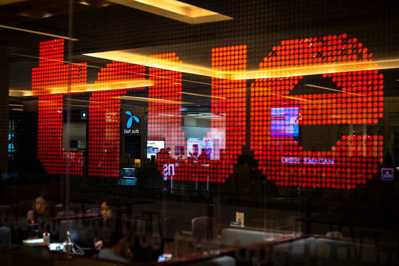 People are silhouetted in front of an electronic screen showing logo of the True Corp. at a department store in Bangkok