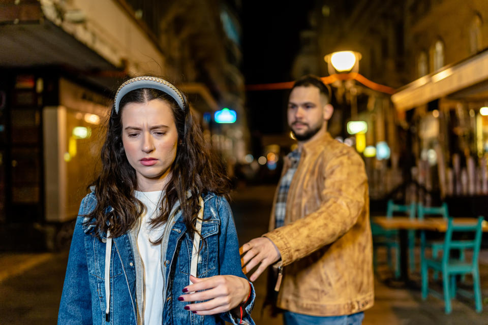 Uncomfortable woman walks away from man reaching out to her on a street at night