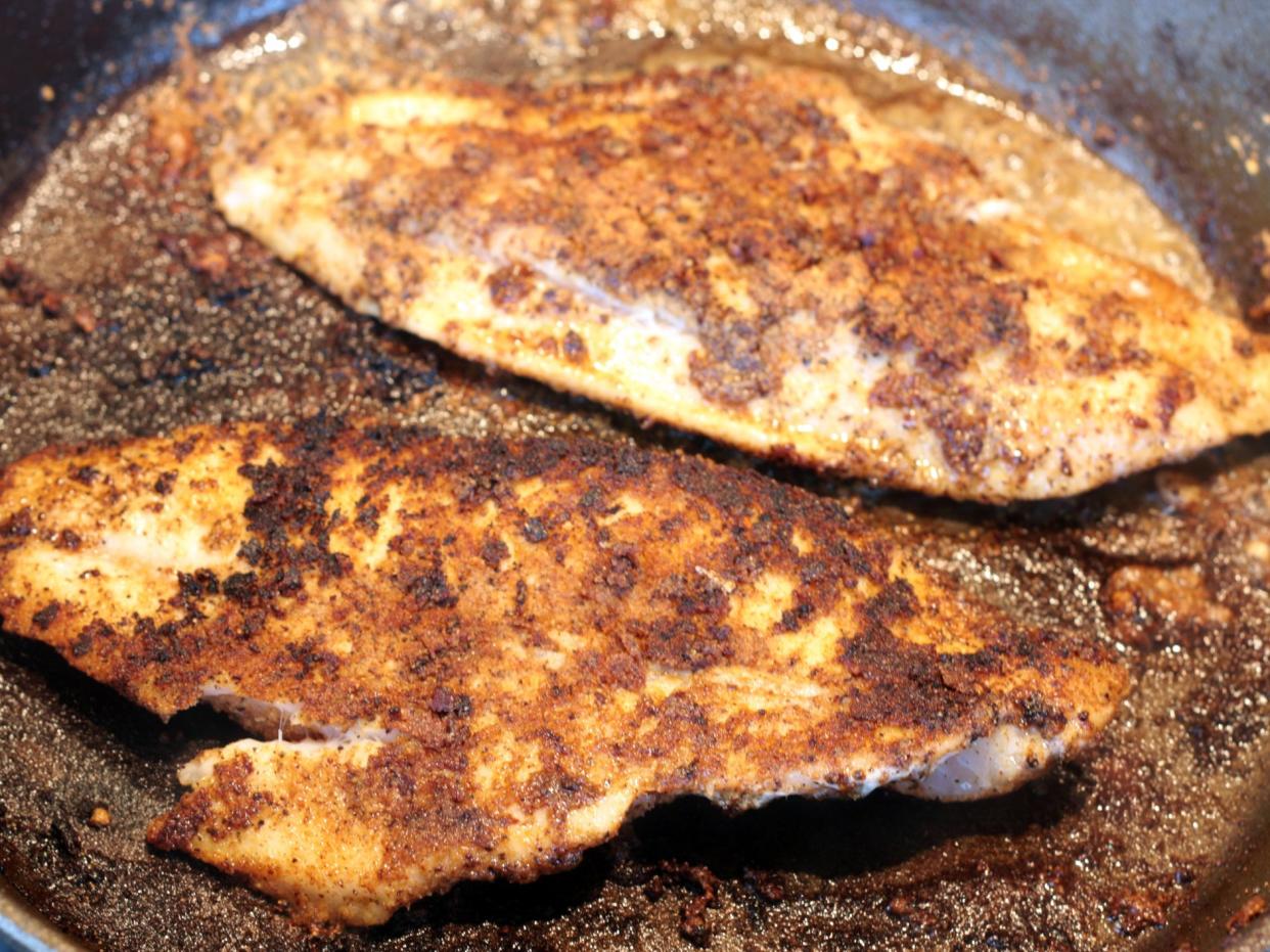 Catfish fillets coated with cajun spice (salt, pepper, garlic powder and cayenne pepper) frying in a cast-iron skillet.
