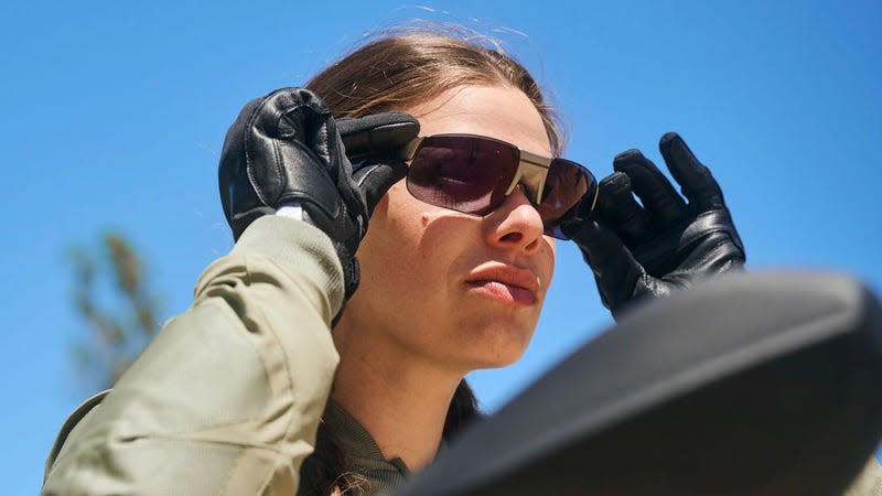 A person on a motorcycle putting on BMW Motorrad's new ConnectedRide Smartglasses while wearing black leather gloves.