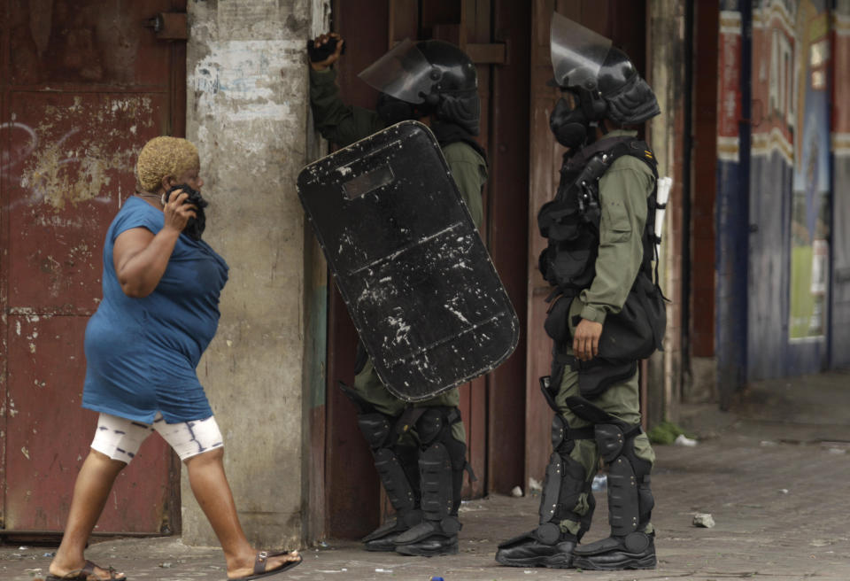 A woman walks past riot police officers during a protest in downtown Colon, Panama, Tuesday, Oct. 23, 2012. Demonstrators protested over a new law allowing the sale of state-owned land in the duty-free zone next to the Panama Canal. Protesters said the land is already being rented and it makes no sense to sell it. They said the government should instead raise the rent and invest the money in Colon, a poor and violent city. (AP Photo/Arnulfo Franco)