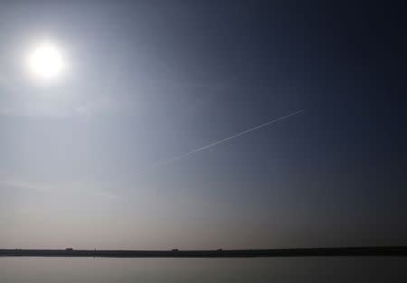 Lorries drive along a levee as they carry earth from the Crossrail project being used to landscape a saltwater marsh wildlife habitat as a passenger jet leaves a vapour trail in the sky on Wallasea island, in Essex, March 13, 2014. REUTERS/Andrew Winning