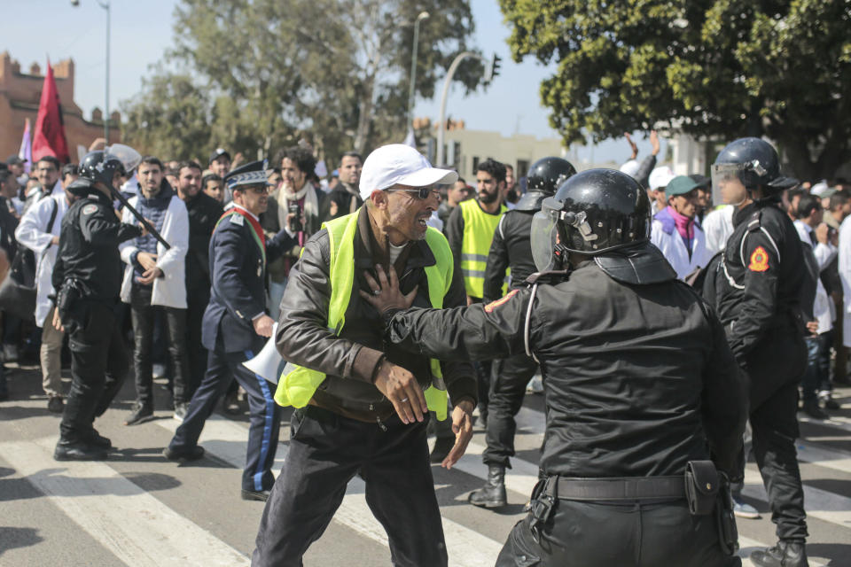 A teacher wearing a yellow vest is confronted by security forces during a demonstration in Rabat, Morocco, Wednesday, Feb. 20, 2019. Moroccan police fired water cannons at protesting teachers who were marching toward a royal palace and beat people with truncheons amid demonstrations around the capital Wednesday. (AP Photo/Mosa'ab Elshamy)