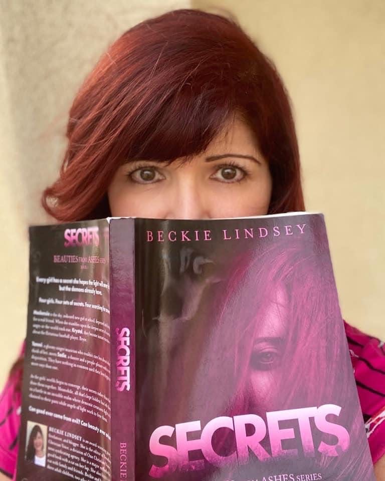 Beckie Lindsey, a local author revered for her inspirational faith-based writings, peeks over the top of her debut novel, “Secrets,” the first in her award-winning young adult series, “Beauties from Ashes.”