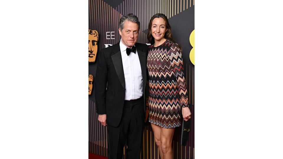 Hugh Grant in a black tuxedo and Anna Eberstein in a patterned dress