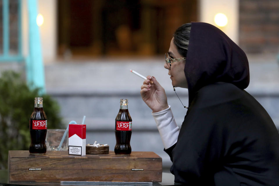 An Iranian smokes a Marlboro cigarette while two Coca-Cola stand on her table at a cafe in downtown Tehran, Iran, Wednesday, July 10, 2019. Whether at upscale restaurants or corner stores, American brands like Coca-Cola and Pepsi can be seen throughout Iran despite the heightened tensions between the two countries. U.S. sanctions have taken a heavy toll, but Western food, movies, music and clothing are still widely available. (AP Photo/Ebrahim Noroozi)