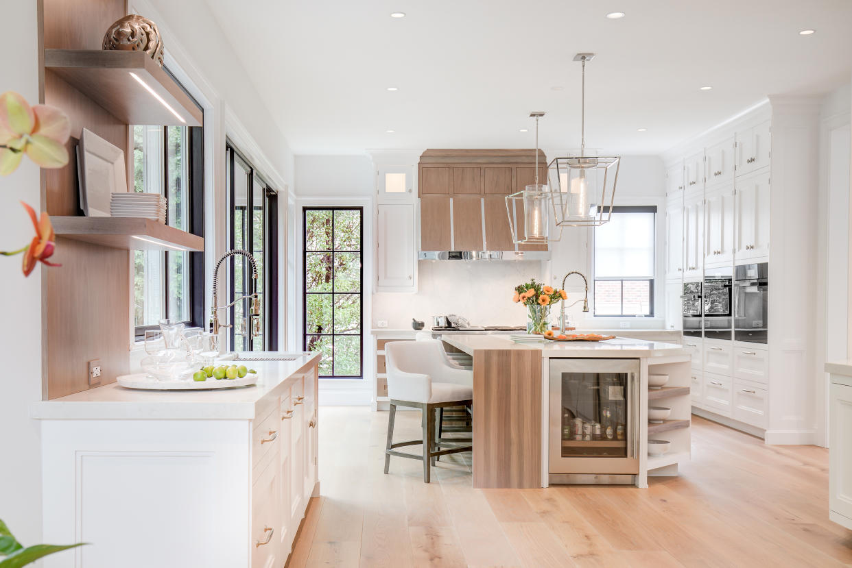  A bright white open plan kitchen with wooden flooring and black framed windows. 