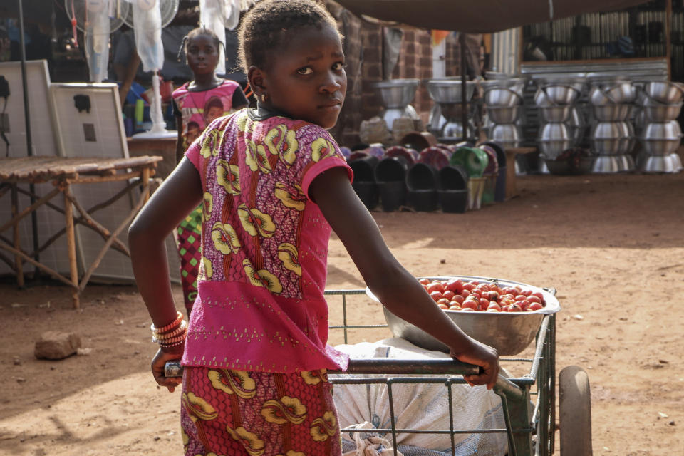 In this Wednesday, May 13, 2020, photo, a girl pushes a cart of food at a market in Tougan, Burkina Faso. Violence linked to Islamic extremists has spread to Burkina Faso's breadbasket region, pushing thousands of people toward hunger and threatening to cut off food aid for millions more. (AP Photo/Sam Mednick)