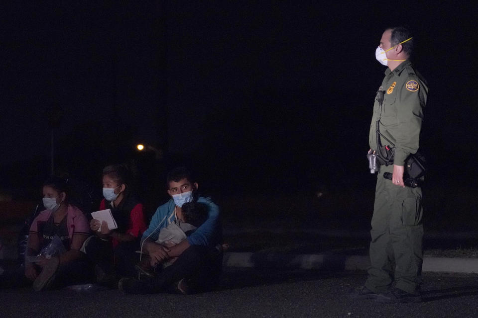 A migrant man, center, holds a child as he looks at a U.S. Customs and Border Protection agent at an intake area after crossing the U.S.-Mexico border, early Wednesday, March 24, 2021, in Roma, Texas. A surge of migrants on the Southwest border has the Biden administration on the defensive. The head of Homeland Security acknowledged the severity of the problem but insisted it's under control and said he won't revive a Trump-era practice of immediately expelling teens and children. (AP Photo/Julio Cortez)