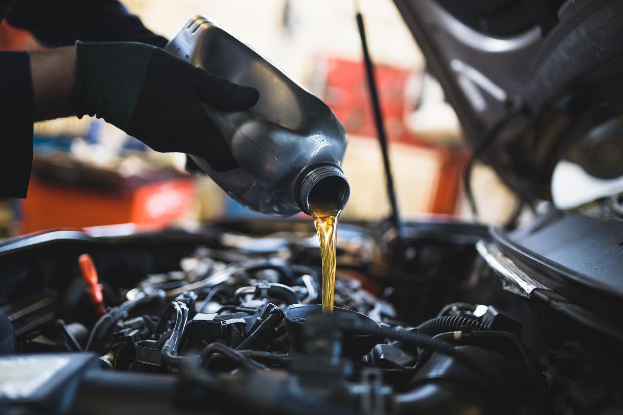 auto mechanic pouring oil into car