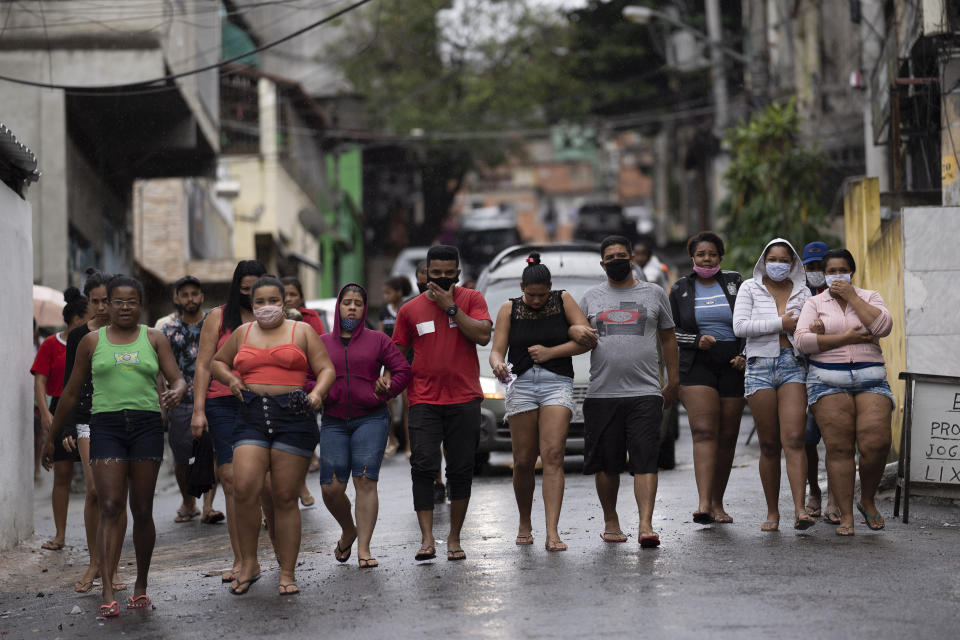 Residents, some wearing masks as a precaution against the spread of the new coronavirus, walk together as they accompany a car transporting the remains of several people who died in an armed confrontation in the Alemao slums complex in Rio de Janeiro, Brazil, Friday, May 15, 2020. According to the civil police, 10 people were found dead during the police operation against alleged drug traffickers. (AP Photo/Leo Correa)