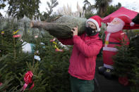 A member of staff at Christmas tree pop-up store wears a face mask to curb the spread of COVID-19 as he arranges christmas trees in London, Monday, Nov. 29, 2021. The new potentially more contagious omicron variant of the coronavirus popped up in more European countries on Saturday, just days after being identified in South Africa, leaving governments around the world scrambling to stop the spread. In Britain, Prime Minister Boris Johnson said mask-wearing in shops and on public transport will be required, starting Tuesday. (AP Photo/Frank Augstein)