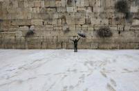 A man holding an umbrella walks as snow falls at the Western Wall in Jerusalem's Old City December 12, 2013. Snow fell in Jerusalem and parts of the occupied West Bank where schools and offices were widely closed and public transport was paused. REUTERS/Ammar Awad (JERUSALEM - Tags: RELIGION ENVIRONMENT)