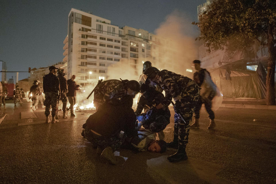 Policemen arrest a Lebanese activist who tried to set himself on fire in protest after security forces ask protesters who have been holding a sit-in in Martyrs Square, to dismantle their tents and go home in line with a nighttime curfew imposed by the government to help stem the spread of the coronavirus in Beirut, Lebanon, Friday, March 27, 2020. The new coronavirus causes mild or moderate symptoms for most people, but for some, especially older adults and people with existing health problems, it can cause more severe illness or death. (AP Photo/Hassan Ammar)