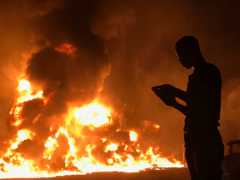 A man stands with his phone in front of flames rising from a pipeline explosion in Abula-Egba, Lagos, Nigeria