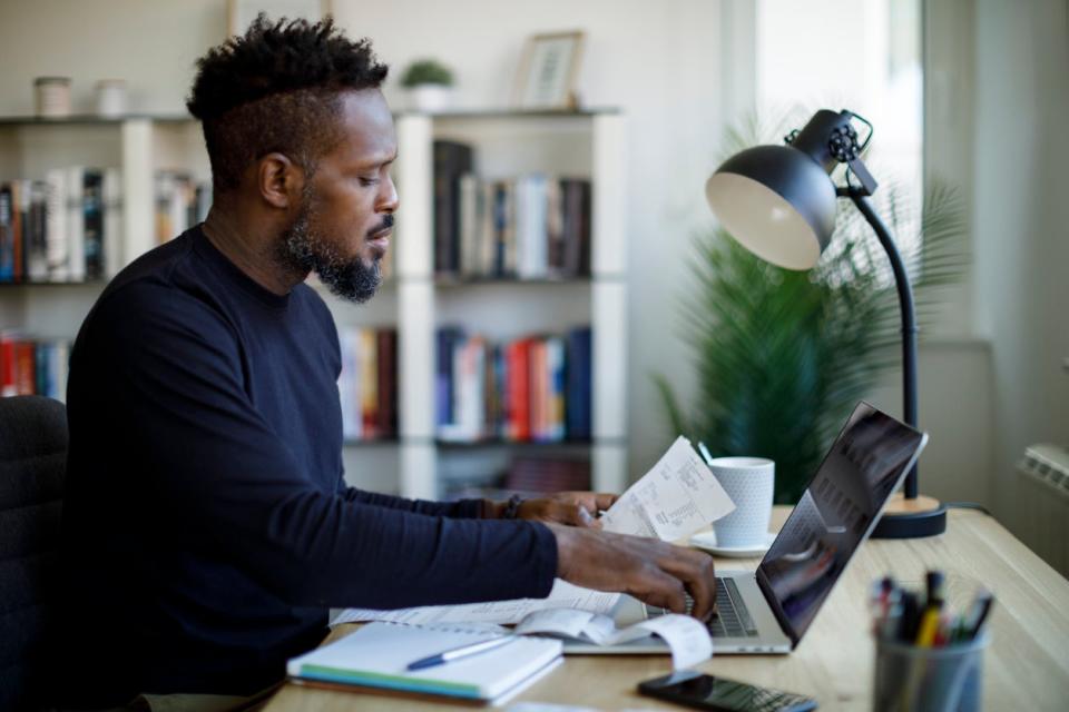 Man holding paper bills working on the computer at his desk at home.